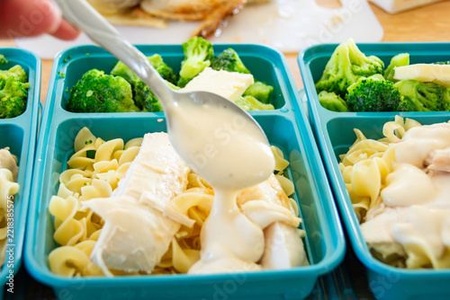 Meal Prep Easy Chicken Alfredo: hand spooning rich white alfredo sauce directly over chicken breast and egg noodles.