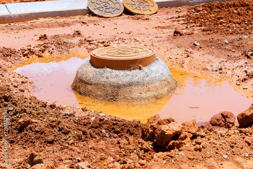Construction site shows manhole cover surrounded by muddy water