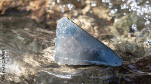 Sharp piece of flint in clear stream with water flowing over its edge, sunlight glinting