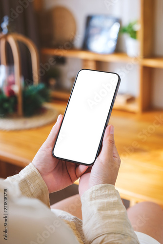 Vertical mockup image of a woman holding and using mobile phone with blank desktop white screen at home