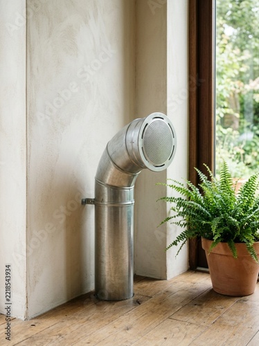 Modern Industrial Interior Design Element Featuring a Galvanized Steel Ventilation Pipe Duct and a Potted Fern Plant on a Rustic Wooden Floor in a Bright Minimalist Living Room with Natural Light
