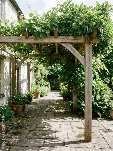 Rustic Wooden Pergola Over Stone Garden Path with Lush Green Climbing Plants and Potted Flowers in a Sunny Countryside Courtyard Setting for Home Decor and Landscape Design Concepts and Backgrounds