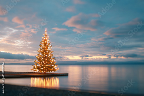 Christmas. New Year. Merry Christmas. Illuminated Christmas tree on a waterfront platform beside calm water beneath a colorful evening sky, realistic coastal holiday scene