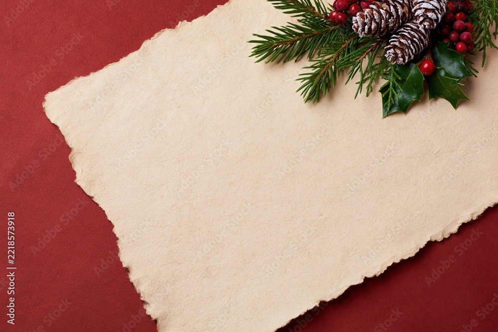 Fototapeta premium The Parchment Sheet with Festive Pinecones and Holly on Red Background