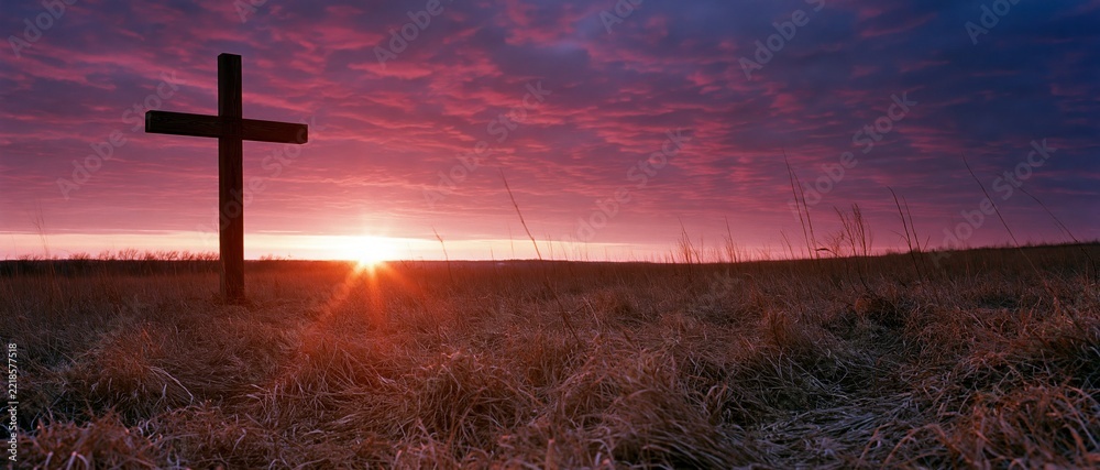 Fototapeta premium Wooden christian cross standing in a grassy meadow at sunset
