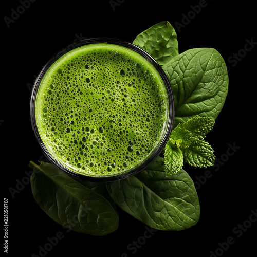 Vibrant green vegetable smoothie in a clear glass with fresh lettuce garnish, isolated on black background, concept of detox