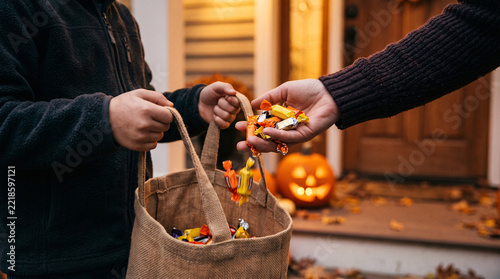 Close-up of adult handing wrapped sweets into jute tote held by child at front door
