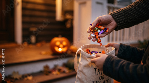 Candy falling into trick-or-treat tote as child holds bag open on porch steps