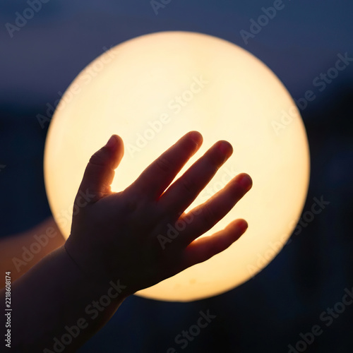 Child's hand reaching for a glowing sphere under a twilight sky. Christmas concept, copy space