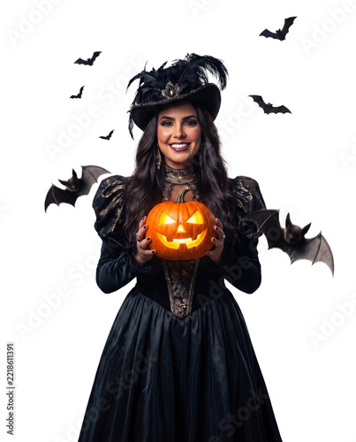 Portrait of a smiling woman in an elegant dark gothic costume holding a glowing jack-o'-lantern with flying bats