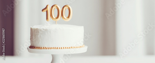 White cake celebrating 100th milestone, golden 100 number on top, marking special birthday or anniversary event