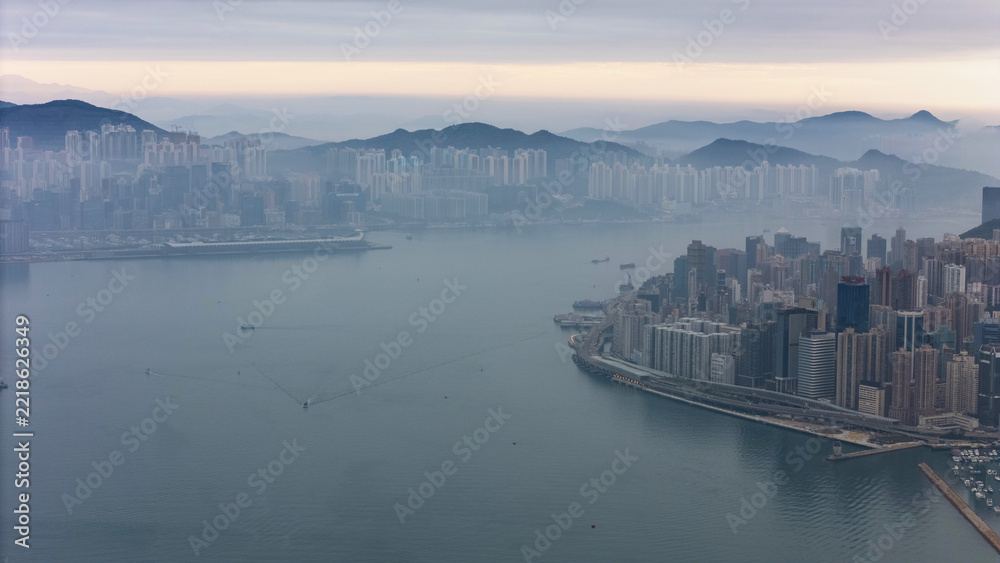 Fototapeta premium Aerial drone view of the eastern end of Hong Kong Island at dawn, with misty mountains behind Kowloon, a wide empty harbour and the city clinging to the narrow shoreline