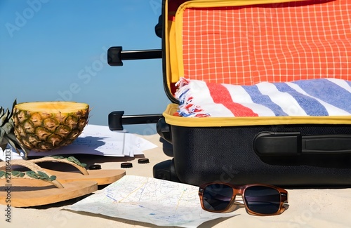 Open travel suitcase packed for vacation with accessories on sandy beach