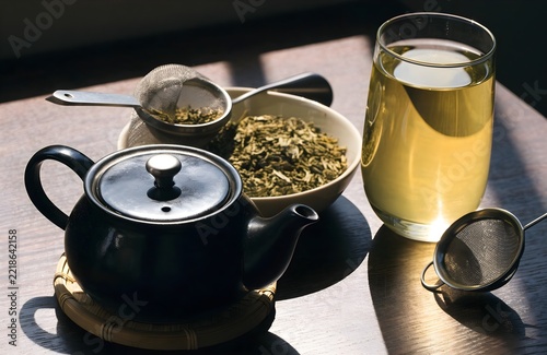 Fresh herbal tea with dark teapot and metal strainer on rustic wooden table
