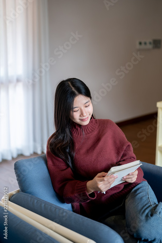 Asian Woman Sitting on Armchair Reading Notebook at Home
