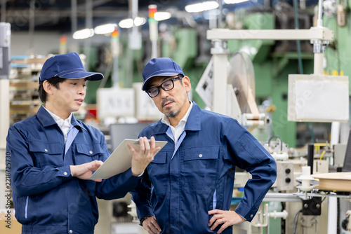製造工場で作業内容を確認する若手男性作業員とベテラン男性作業員