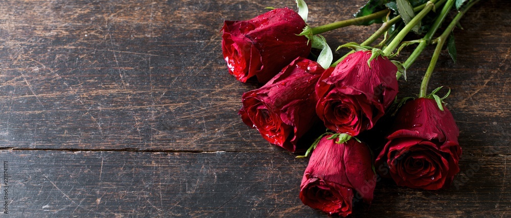 Naklejka premium Five red roses with water droplets arranged on a dark wooden table