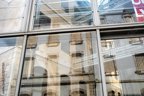 Reflections in a glass facade reveal older buildings and create abstract architecture where transparency layers and textures merge across the glass facade