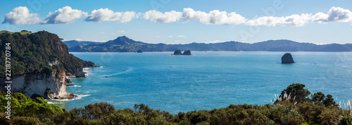 Rugged white cliffs covered in dense greenery rise above the deep blue ocean in Coromandel, with rocky sea stacks and distant hills completing the scenic coastal view