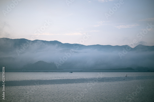 Deep morning fog covering mountain slope over calm sea at dawn