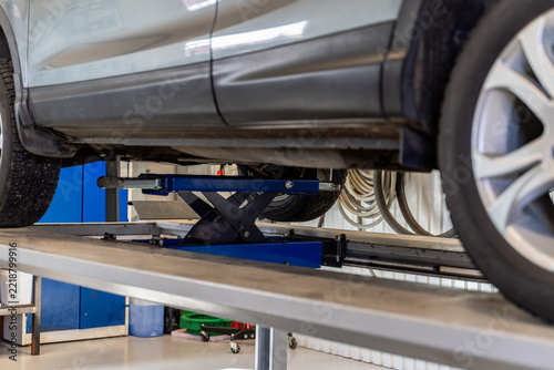 Silver SUV raised on a scissor lift in a car workshop, side view with studded winter tires, alloy wheel and coiled air hoses on the wall