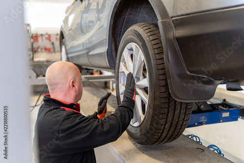 Mechanic holds a car wheel with alloy rim next to an SUV on a lift during a tire change in a garage