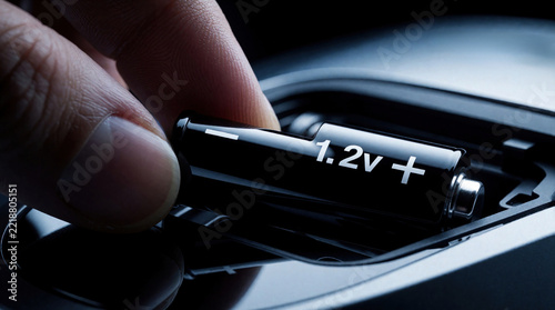 Close up of person hand inserting black rechargeable battery into electronic device. Human finger places 1. 2v energy cell into battery compartment. Power supply connection for portable tech gadget,