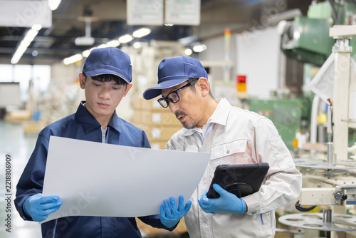 製造工場で図面を確認しながら打ち合わせをする日本人のベテラン技術者と外国人男性労働者