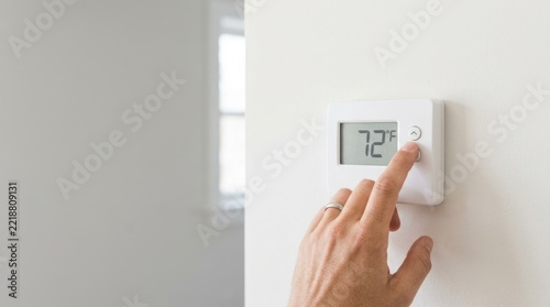 Hand adjusting thermostat temperature on a white wall. Smart home climate control and energy saving
