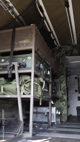 Vertical screen Military transport vehicle interior with organized storage racks holding tactical gear equipment cases and supplies secured for safe transportation and field operations