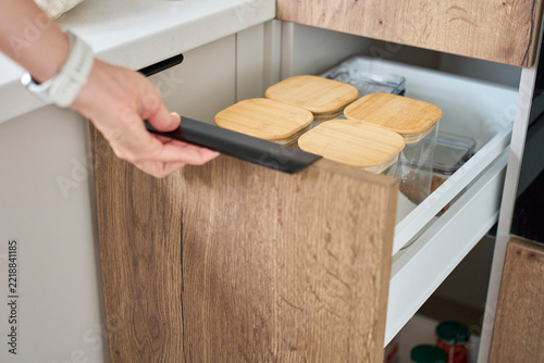 Hand opening kitchen drawer filled with transparent food storage containers
