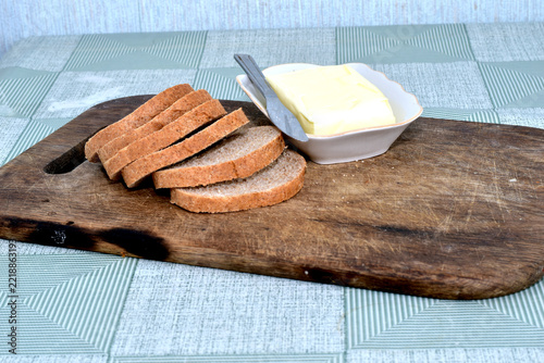 Slices of bread lie on a cutting board, and a plate of butter sits there.