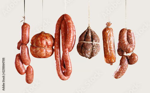 Assortment of different cured sausages hanging on white background