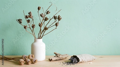 Minimalist home decor featuring a white ceramic vase with dried branches and poppy heads on a wooden table
