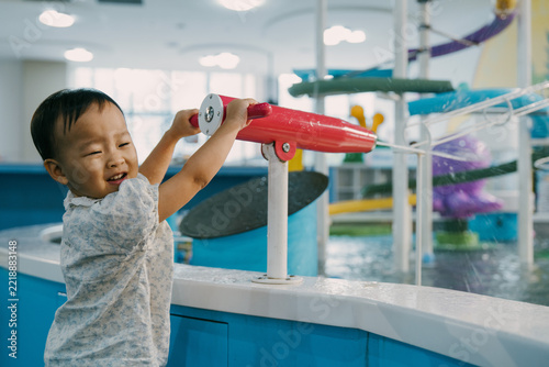 An Asian girl is playing with a water gun in an indoor amusement park; Asian families are enjoying a relaxing family trip