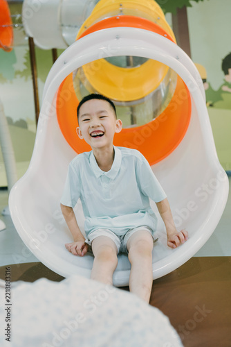 An Asian boy and his sister are playing on the slide in an indoor amusement park; an Asian family is enjoying a relaxing vacation