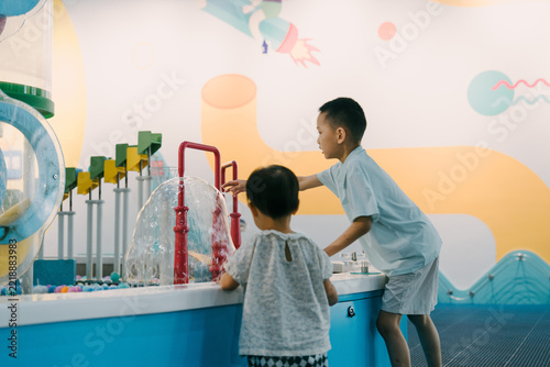 An Asian girl and her brother are playing with water guns in an indoor amusement park; an Asian family is enjoying a relaxing family trip
