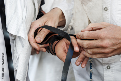 Jewish man wrapping tefillin straps around his arm and hand during morning prayer.