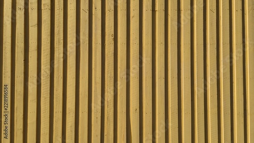 Wooden wall with yellow paint and vertical lines in sunlight