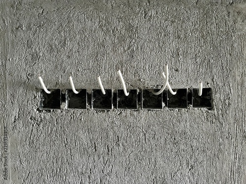 Electrical flush mounted socket junction boxes with installed white cables on unfinished concrete wall during house renovation