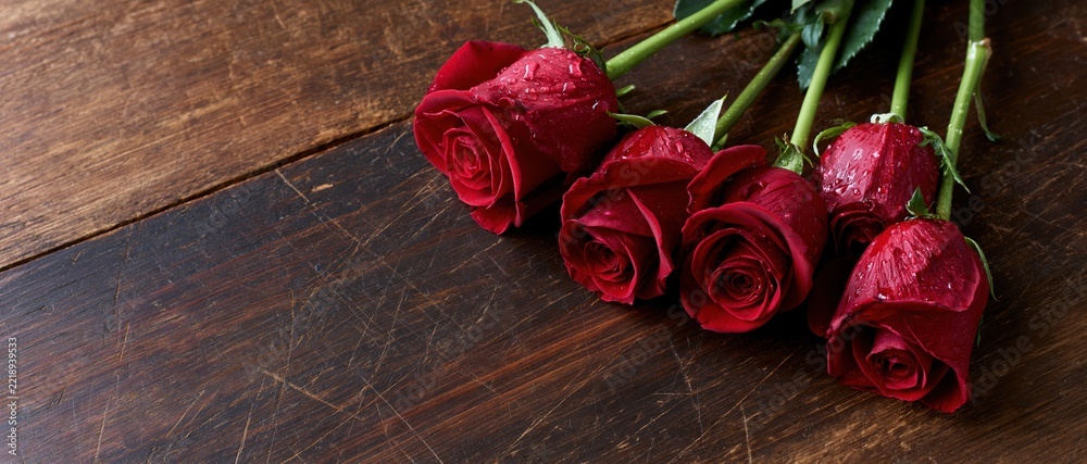 Naklejka premium Five red roses with water droplets arranged on a dark wooden surface