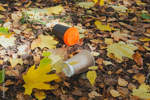 Discarded disposable coffee cups lying as trash on autumn foliage.
