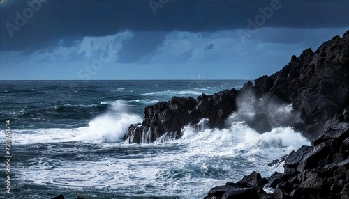 Dark stormy ocean waves crashing against jagged black volcanic rocks on a cloudy coastline during high tide