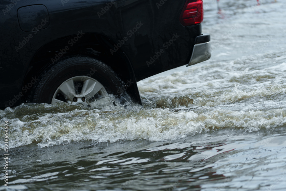 Naklejka premium A vehicle is driving through deep floodwaters on the road. 