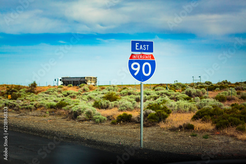 East interstate 90 sign, by the road, an exit sign, and a freighter on the road ahead.