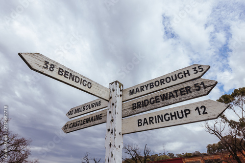 Historic wooden directional road fingerpost pointing to regional Victorian towns under cloudy sky