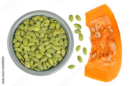 Peeled pumpkin seeds in ceramic bowl with piece of pumpkin isolated on white background. Top view. Flat lay