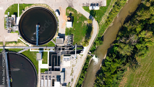 Aerial view of Depuratore di Truccazzano with circular sedimentation tanks and water treatment infrastructure next to a river and green fields in Truccazzano, Lombardia, Italy.