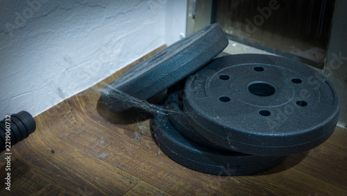 Adjustable dumbbell handle with weight plates: A close-up shot of an adjustable dumbbell handle with a spiderweb clinging to it.