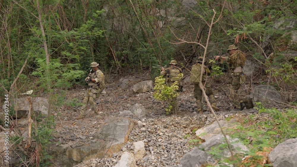 Fototapeta premium A squad of elite soldiers in full tactical gear carefully advances through a rugged jungle environment on a covert reconnaissance mission, displaying teamwork and vigilance.